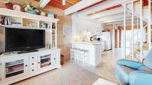Un soggiorno moderno con televisione a schermo piatto, mobili bianchi, un divano blu e un angolo cucina sullo sfondo.