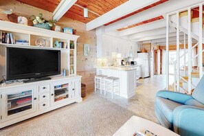 A modern living room with a flat-screen TV, white cabinetry, a blue sofa, and a kitchen area in the background. - Caravelle 5 (Ocean City)