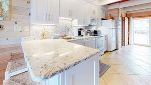 Una cucina moderna con mobili bianchi, un piano di lavoro in marmo e un soffitto in legno.
