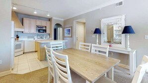 A modern kitchen with white cabinets, a dining area with a wooden table and chairs, and a small island with seating. - Roomy & convenient bayfront home with pool, central AC & balcony (Ocean City)