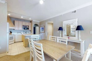 A modern kitchen with white cabinets, a dining area with a wooden table and chairs, and a small island with seating. - Roomy & convenient bayfront home with pool, central AC & balcony (Ocean City)