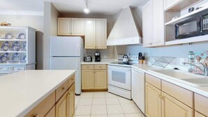 A compact kitchen with white cabinets, a refrigerator, a stove, and a microwave. - Roomy & convenient bayfront home with pool, central AC & balcony (Ocean City)