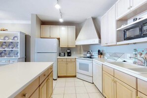 A compact kitchen with white cabinets, a refrigerator, a stove, and a microwave. - Roomy & convenient bayfront home with pool, central AC & balcony (Ocean City)