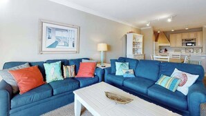 A living room with two blue sofas, a white coffee table, and a kitchen in the background. - Roomy & convenient bayfront home with pool, central AC & balcony (Ocean City)