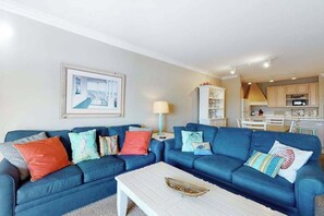 A living room with two blue sofas, a white coffee table, and a kitchen in the background. - Roomy & convenient bayfront home with pool, central AC & balcony (Ocean City)