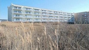 A multi-story building with balconies, likely a hotel or apartment complex, surrounded by dry grass. - Roomy & convenient bayfront home with pool, central AC & balcony (Ocean City)