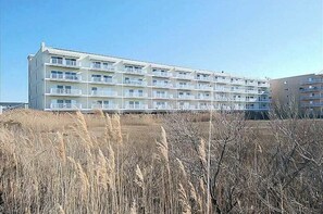 A multi-story building with balconies, likely a hotel or apartment complex, surrounded by dry grass. - Roomy & convenient bayfront home with pool, central AC & balcony (Ocean City)