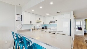 Cozinha moderna com armários brancos, uma ilha central, banquetas azuis, micro-ondas e fogão.