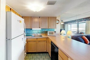 A compact kitchen with wooden cabinets, a white refrigerator, a microwave, and a dishwasher. - Irene 404 (Ocean City)