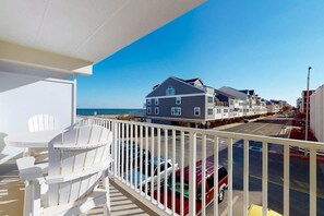 A balcony with white chairs, a view of a coastal building, and parked cars. - Ocean Block Condo w/ Balcony, Side Ocean View, AC, WiFi & Shared Pool (Ocean City)