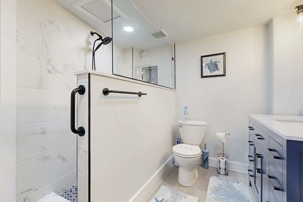 A bathroom with a glass shower enclosure, a toilet, a sink, and a mirror.