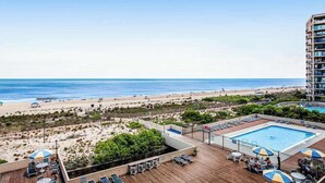 Zona de piscina en la azotea con sillones de descanso y sombrillas, con vistas a una playa y el océano.