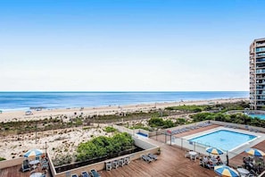 Ein Poolbereich auf dem Dach mit Liegestühlen und Sonnenschirmen mit Blick auf einen Strand und das Meer.