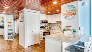 Una cocina moderna con armarios blancos, techo de madera y un reloj en la pared.