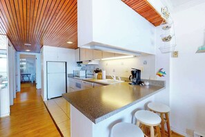 A modern kitchen with a central island, white cabinetry, and a wooden ceiling. - Oceanfront condo with balcony, AC, pool, & W/D (Ocean City)
