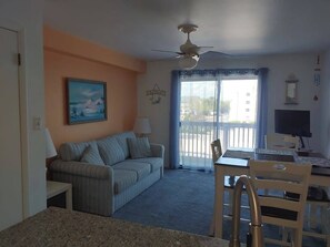 A living room with a sofa, a dining table with chairs, a ceiling fan, and a window with curtains. - Two-level condo with balcony, AC, pool & dock - blocks to beach/Northside Park (Ocean City)
