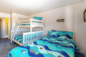 Ein Schlafzimmer mit Etagenbetten, einer blau gestreiften Bettdecke im Meeresstil, weißen Geländern und einer kleinen Wanddekoration.