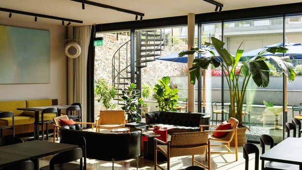 Un intérieur moderne avec un escalier, des coins salon et de grandes fenêtres.