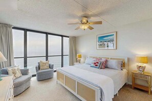 A hotel room with a large window, a bed, a ceiling fan, and a nightstand with a lamp. - Bright waterfront condo with balcony, incredible views, pools & gym (Ocean City)