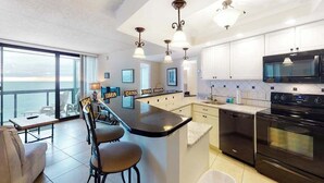 Una cocina moderna con una isla grande, electrodomésticos negros y vistas al océano.