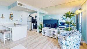 Una sala de estar moderna con cocina, un televisor de pantalla plana grande y una zona de estar con sofá estampado.