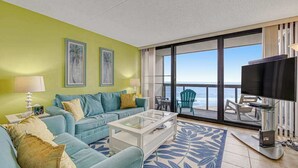 Un soggiorno con divano, tavolino e televisore. Include un balcone con vista sull'oceano.