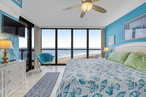 Ein Schlafzimmer mit Bett, Deckenventilator, Fernseher, Stuhl und Blick auf den Strand.