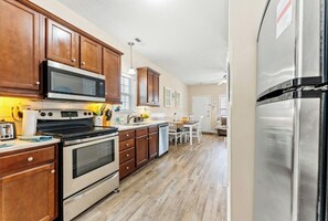 A kitchen with wooden cabinets, a stainless steel refrigerator, and a dining area with a table and chairs. - Gulf Stream Cottages 1928-walk to beach (Myrtle Beach)