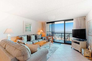 A living room with a sofa, coffee table, TV, and balcony with chairs. - Updated beachfront condo, high speed internet, balcony, pools & AC (Ocean City)