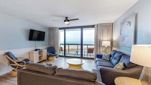 Ein modernes Wohnzimmer mit einer Couch, Sesseln, einem Fernseher und einem Balkon mit Blick.