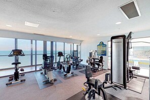 A gym with various exercise equipment, large windows, and a view of the ocean. - Joyful beachfront condo with balcony, pools, gym, game room & AC (Ocean City)