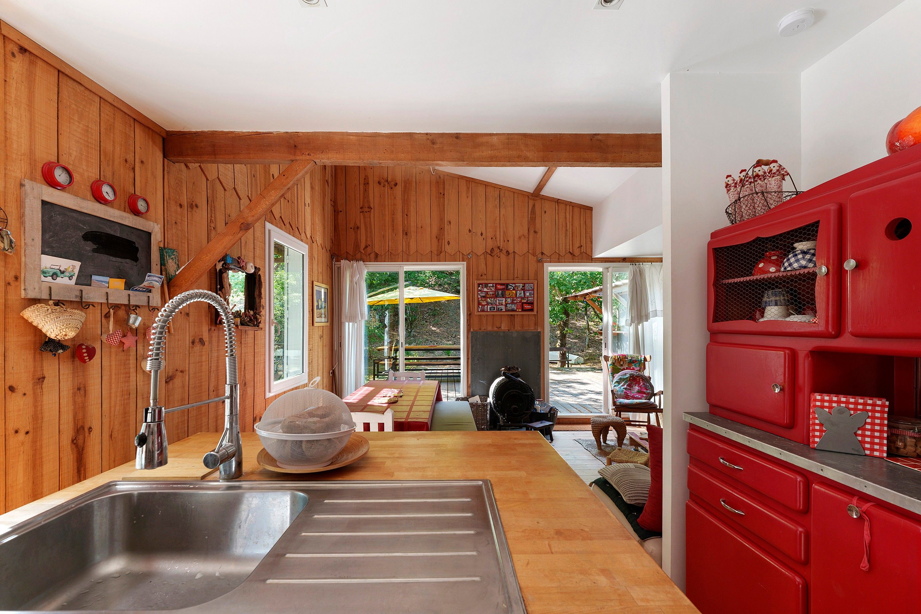 Une cuisine avec des murs en bois, un évier en acier inoxydable, un meuble rouge et un coin repas comprenant une table et des chaises.