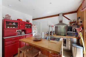 A kitchen with a wooden island, red cabinets, stainless steel appliances, and a hanging pot rack. - Holiday Home "Cabane Eden Pyla" with Private Terrace and Garden (La Teste-de-Buch)