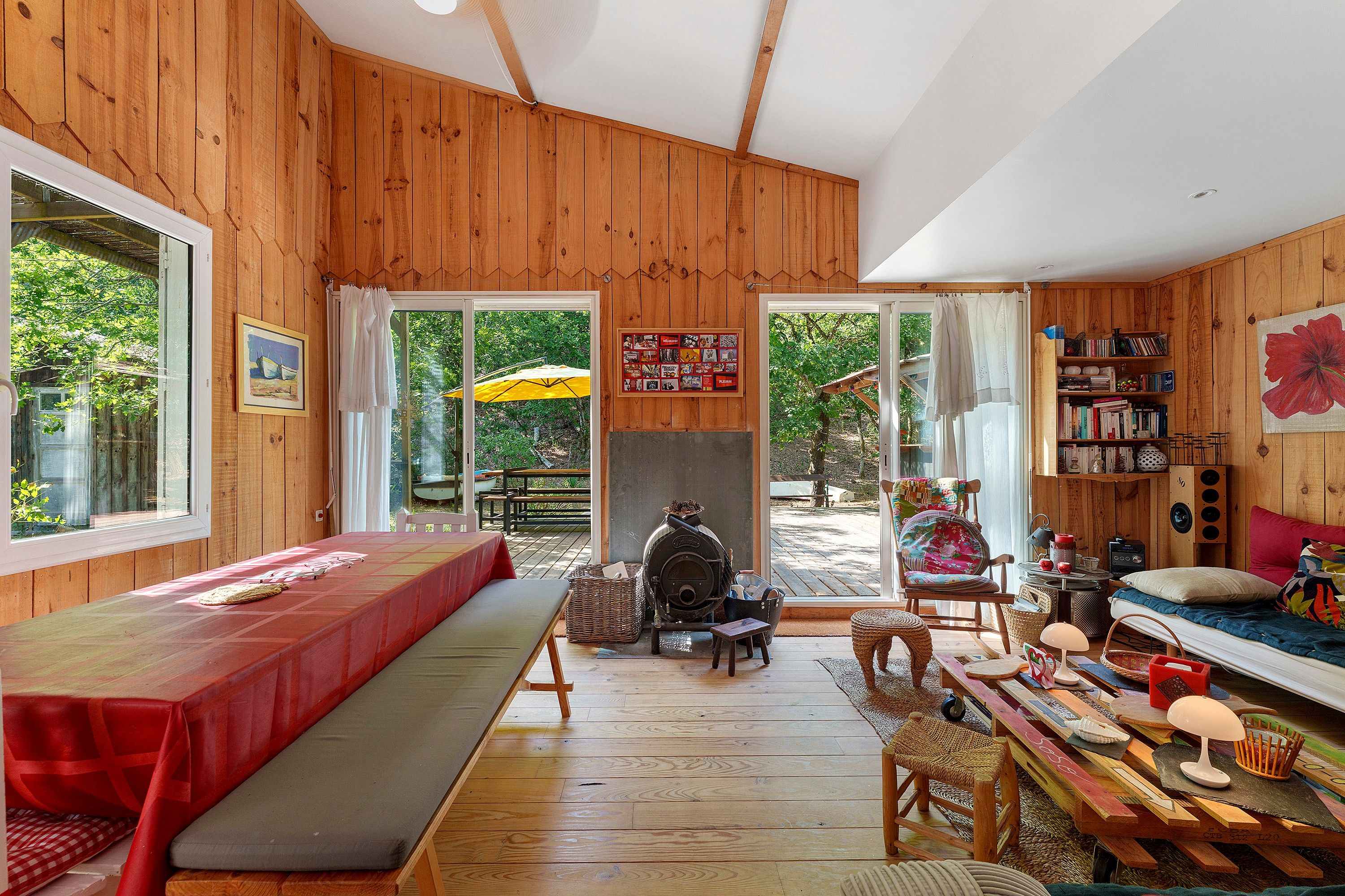 Een gezellig houten huisje met een lange bank, een open haard, een boekenkast en uitzicht op de natuur.