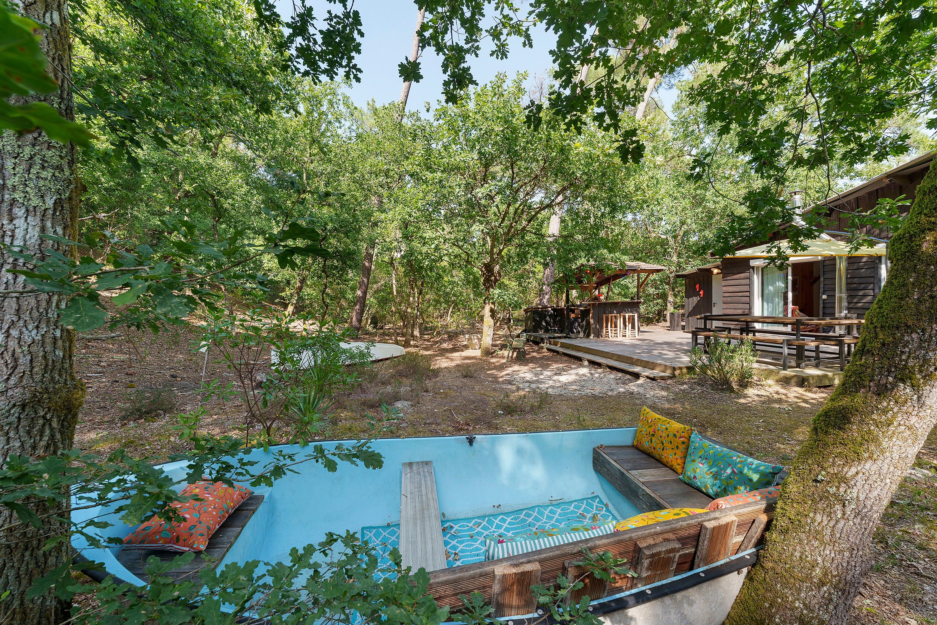 Ein Poolbereich mit Holzterrasse, umgeben von Bäumen und einer Holzhütte.