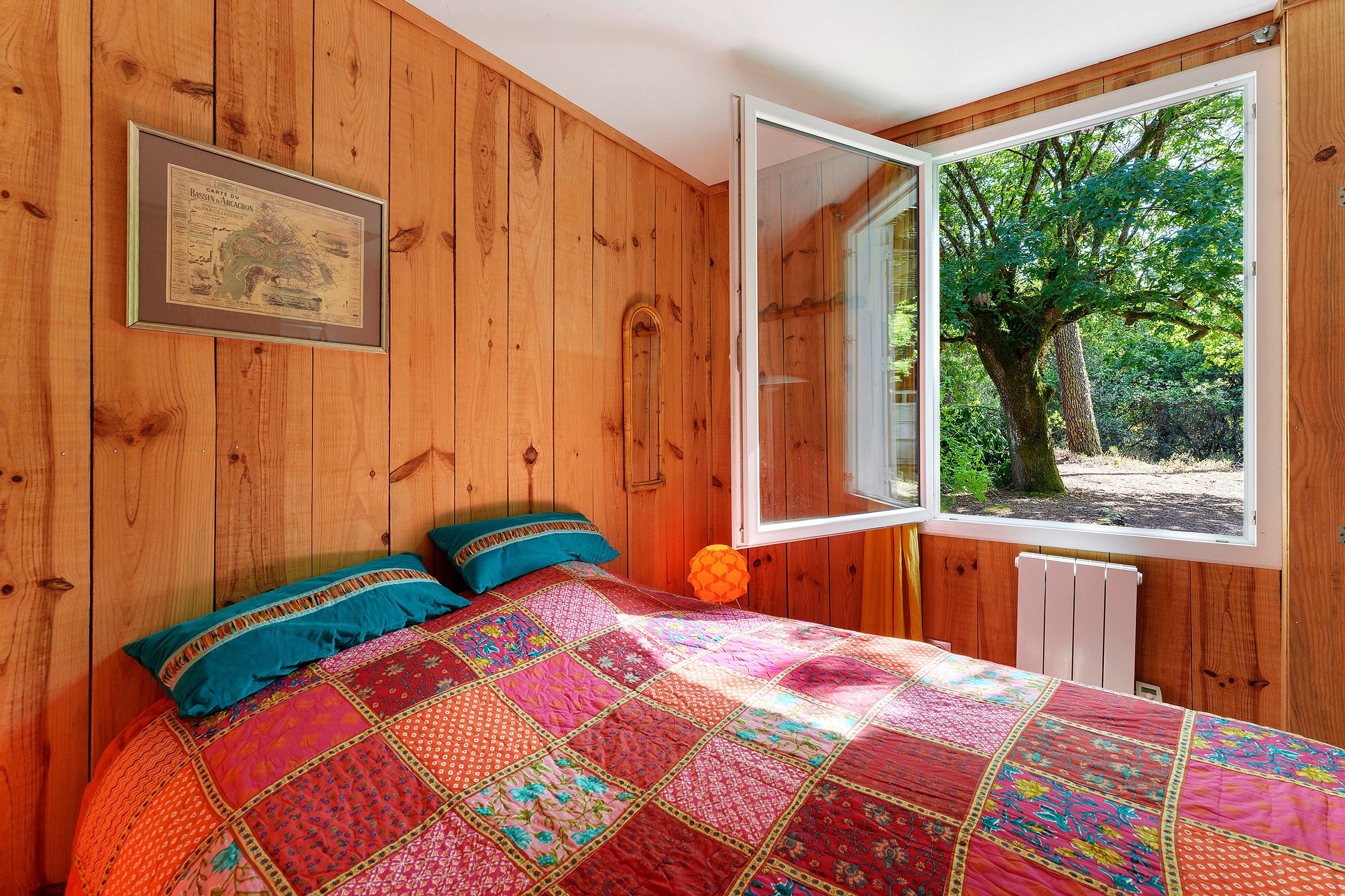 Een kamer met houten lambrisering, een bed, een raam en een lijst met een kaart aan de muur.
