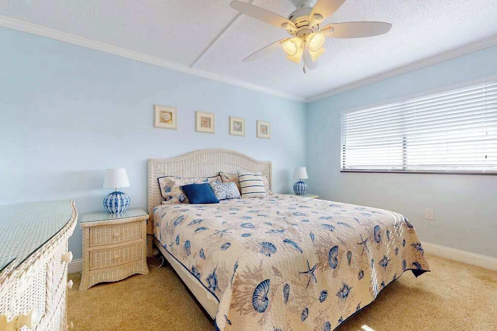 A bedroom with a bed, nightstands, a ceiling fan, and a window with blinds.