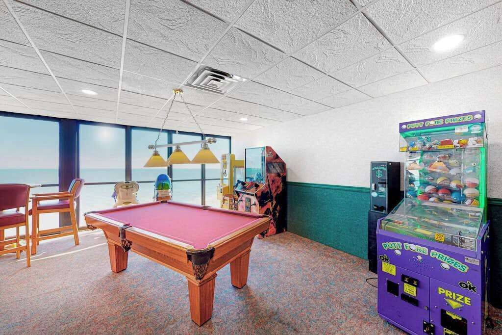 A pool table, chairs, a claw machine, and a view through large windows.