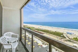 A balcony with white chairs, a view of the beach, and outdoor seating with umbrellas. - Stunning beachfront condo with beach-view balcony, pools, tennis & gym (Ocean City)