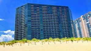 Un moderno edificio de gran altura con una rejilla de balcones, ubicado junto a una playa de arena.
