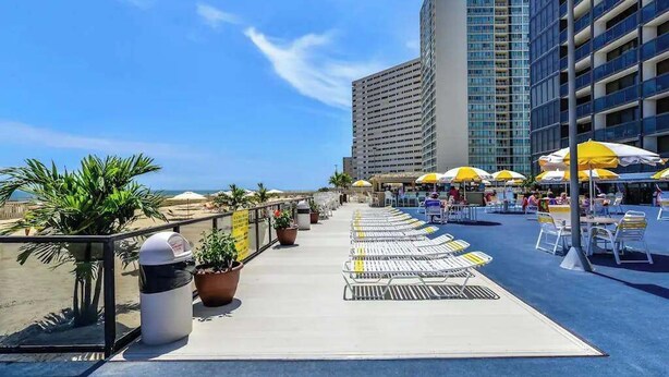 A rooftop terrace with sun loungers, umbrellas, and potted plants. - Remodeled condo with beach views, balcony, pools, gym, tennis & AC (Ocean City)