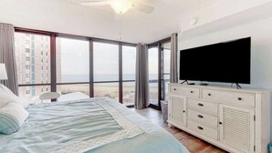 A bedroom with a bed, a television, a ceiling fan, and a large window with a view. - Remodeled condo with beach views, balcony, pools, gym, tennis & AC (Ocean City)