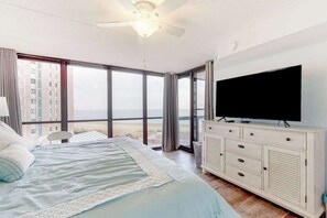 A bedroom with a bed, a television, a ceiling fan, and a large window with a view. - Remodeled condo with beach views, balcony, pools, gym, tennis & AC (Ocean City)