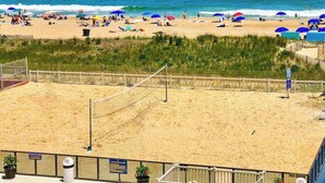 A beach volleyball court with a net, surrounded by sand and a wooden fence. - Remodeled condo with beach views, balcony, pools, gym, tennis & AC (Ocean City)