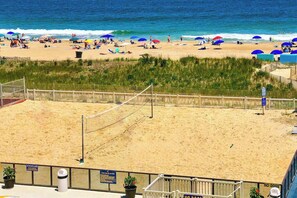 A beach volleyball court with a net, surrounded by sand and a wooden fence. - Remodeled condo with beach views, balcony, pools, gym, tennis & AC (Ocean City)
