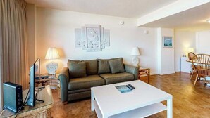 A living room with a sofa, a coffee table, a TV, and a lamp. - Fountainhead Towers 1204 (Ocean City)