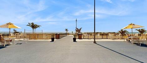 A beachside promenade with sun loungers and umbrellas, a clear sky, and a view of the ocean.