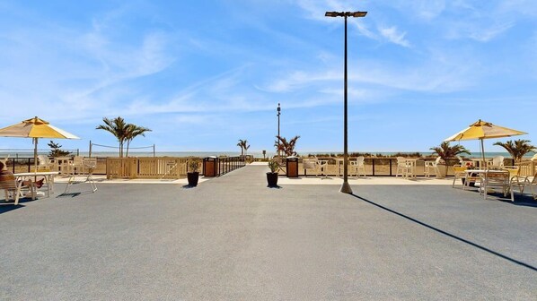 Eine Strandpromenade mit Liegestühlen und Sonnenschirmen, einem klaren Himmel und Blick auf den Ozean.