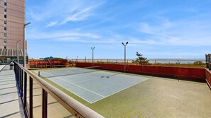 Ein Tennisplatz im Freien mit freiem Blick auf das Meer, umgeben von einem roten Zaun und Laternen.