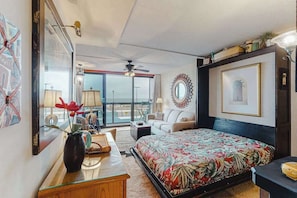 A bedroom with a bed, a desk, a chair, a sofa, a ceiling fan, and a view of the outside. - Convenient studio right on the beach with pools & W/D (Ocean City)